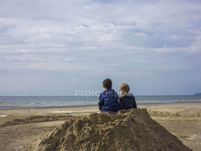 Normandie, Deux enfants sur la plage vus de derrière sur un tas de sable — Photo de stock