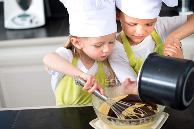 Two young kids happy childrens boy and girl family with apron and chef hat preparing funny cookies in kitchen at home. — Stock Photo