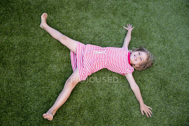 Vue d'une jolie petite fille faisant la star sur une pelouse verte. — Photo de stock