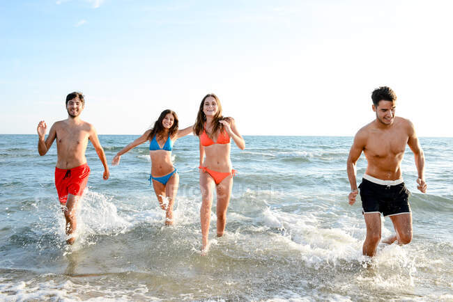Francia, quattro giovani adulti che corrono in mare in costume da bagno. — Foto stock