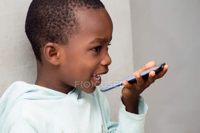 Este niño habla directamente en el micrófono del teléfono móvil junto con una hermosa sonrisa . - foto de stock