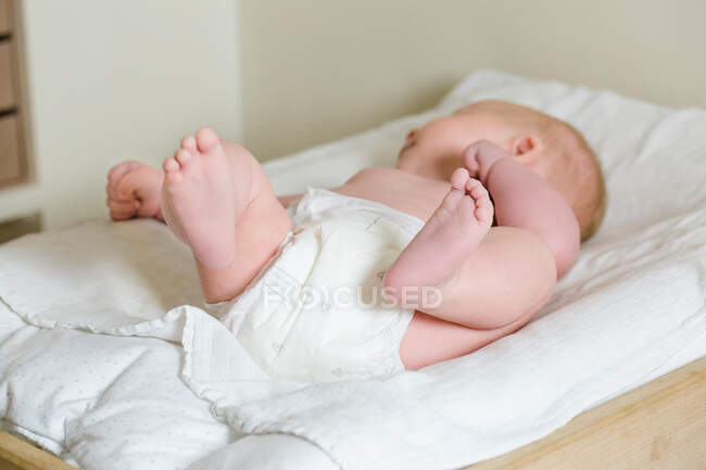 Bebé 2 meses acostado boca arriba con los pies en un cambiador. - foto de stock