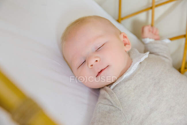 Cara sorridente de um bebê de 2 meses dormindo de costas em sua cama. — Fotografia de Stock