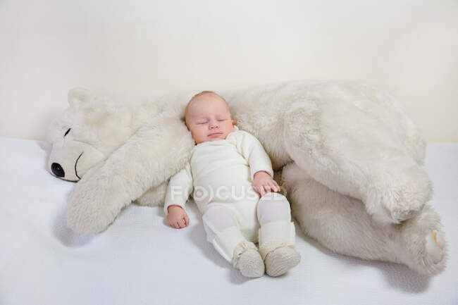View of a young infant sleeping with a huge white teddy bear on a bed. — Stock Photo