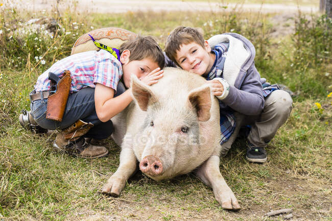 Dos niños abrazando a un cerdo, Rancho La Joya, Rancho John Wayne, Durango, México, Centroamérica - foto de stock