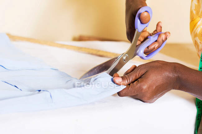 A seamstress cutting a piece of cloth on his table. — Stock Photo