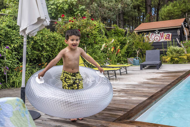 Garçon de 6 ans jouant avec ann flotteur gonflable sur la terrasse de la piscine — Photo de stock