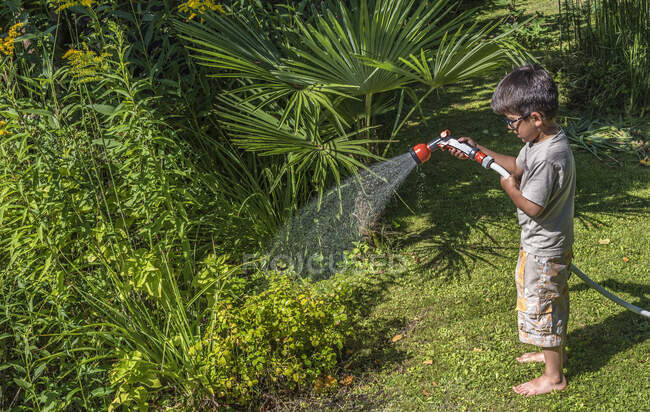 Garçon de cinq ans arrosant les plantes avec un tuyau — Photo de stock
