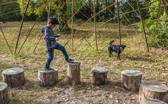 Ragazzo di sette anni che gioca su tronchi di legno in un parco pubblico — Foto stock