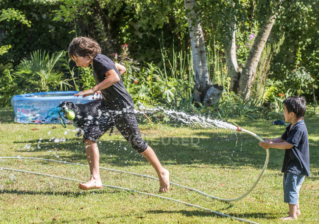 Due ragazzi di 4 anni e 12 anni che giocano con un tubo in giardino — Foto stock