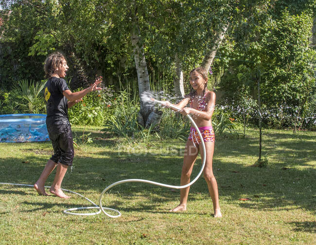 Deux garçons de 4 ans et 12 ans et une fille de dix ans jouant avec un tuyau dans le jardin — Photo de stock