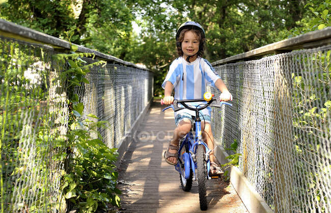 Six-year-old boy cycling on a bridge in the forest — Stock Photo