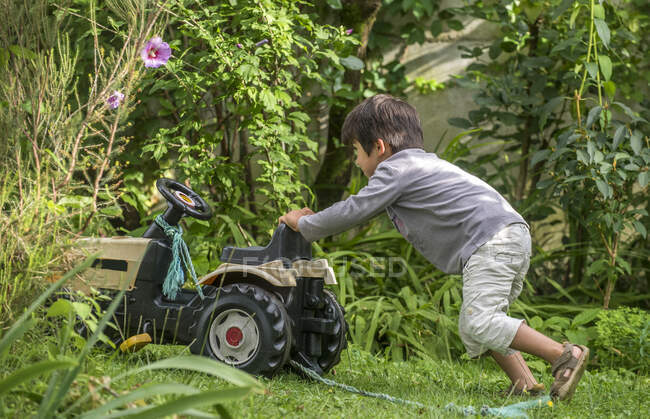 Four-year-old boy in the garden, pushing his toy tractor — Stock Photo