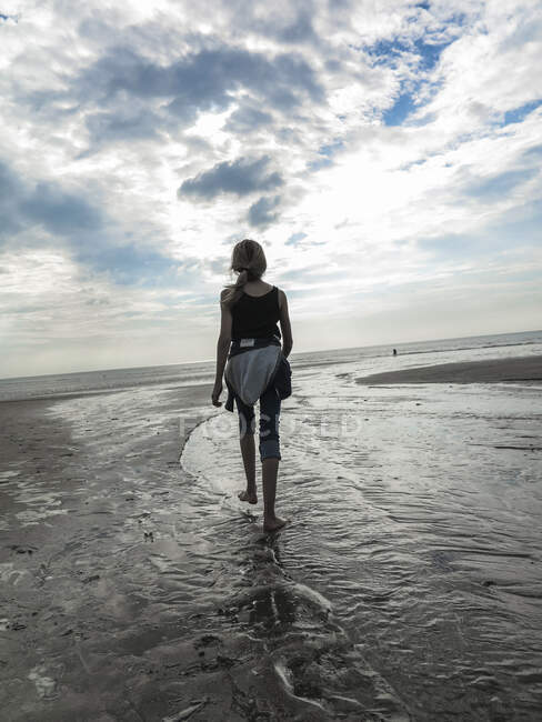Jovencita vista desde atrás caminando en una playa - foto de stock