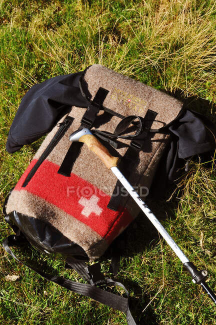 Suiza, cantón de Berna, región de Hight-Simmental, primer plano en una mochila hecha de fieltro con la cruz suiza en ella y de un bastón puesto en la hierba - foto de stock