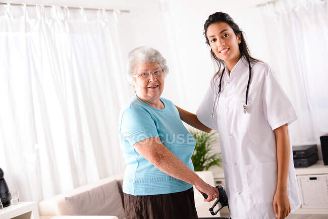Joyeuse jeune infirmière de désintox aidant femme âgée âgée à l'aide d'un marcheur — Photo de stock