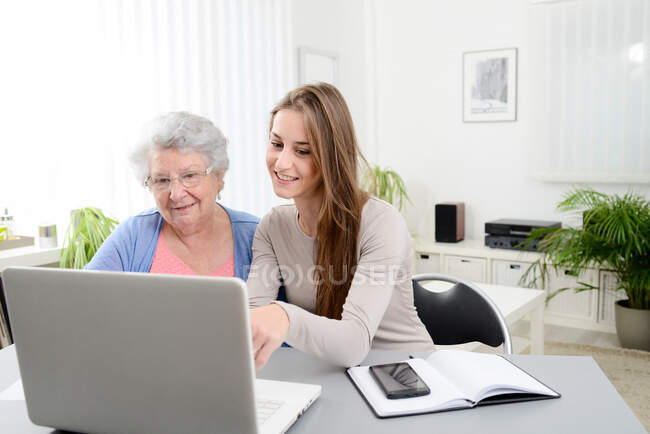 Young woman helping old senior woman doing paperwork and administrative procedures with laptop computer at home — Stock Photo