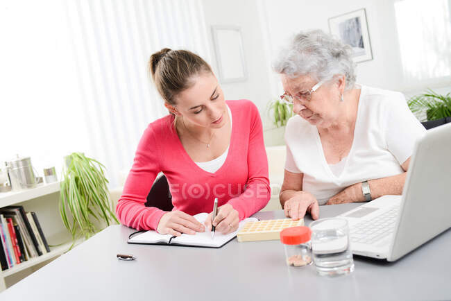 Joven alegre ayudando a la mujer mayor con pastillas de prescripción médica - foto de stock