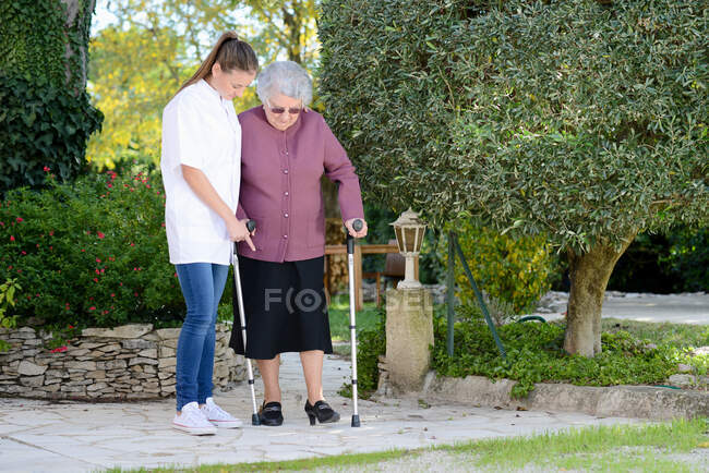 Elderly senior woman with a nurse walking outdoor in nursing home hospital garden — Stock Photo