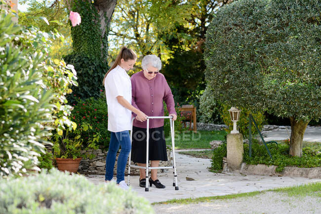 Anciana mujer mayor con una enfermera caminando al aire libre en casa de ancianos hospital jardín - foto de stock