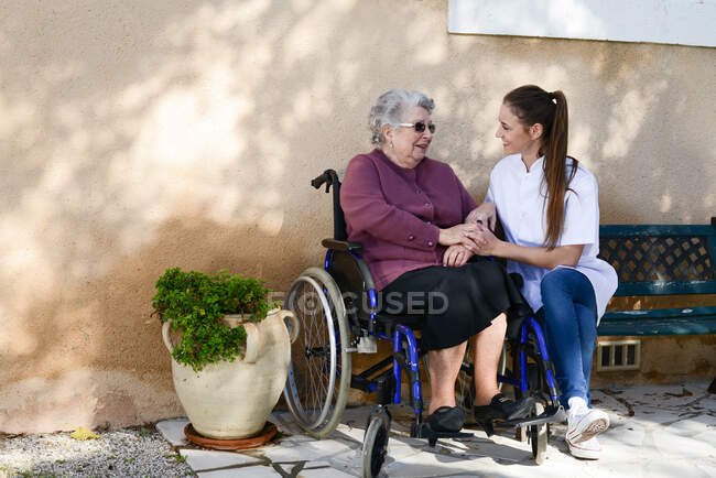 Ältere Seniorin im Rollstuhl mit Krankenschwester im Garten des Pflegeheims. — Stockfoto