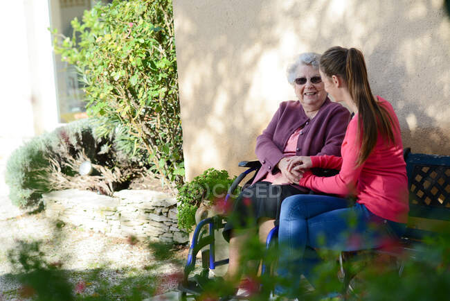 Fröhliche junge Frau im Garten eines Altenheims mit einer älteren Seniorin. — Stockfoto