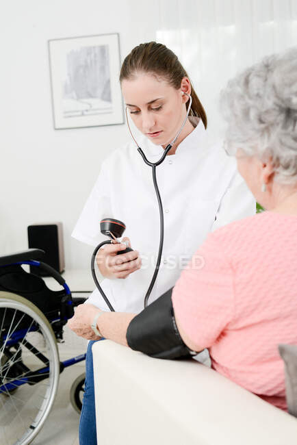 Femme âgée âgée avec jeune médecin recevant des soins médicaux à domicile. — Photo de stock