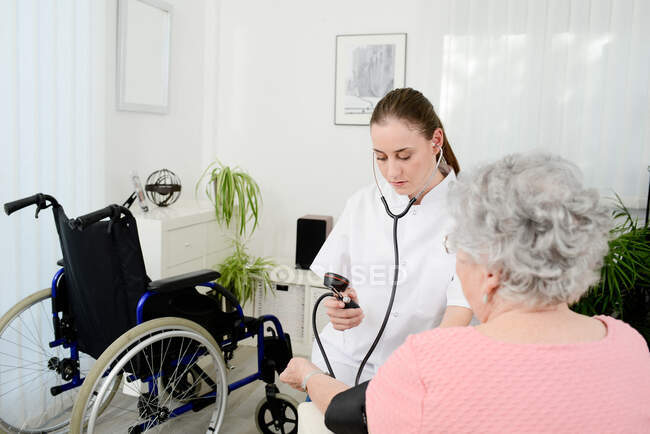 Femme âgée âgée avec jeune médecin recevant des soins médicaux à domicile. — Photo de stock