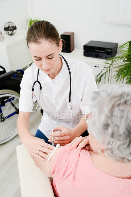 Joyeux jeune femme médecin donnant injection de vaccin à la femme âgée à la maison. — Photo de stock