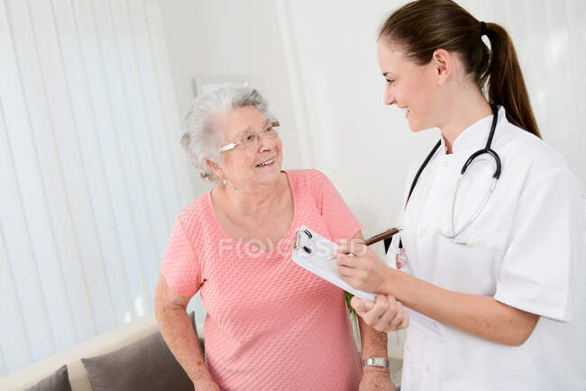 Jeune médecin vérifiant les progrès médicaux de réadaptation à la femme âgée à la maison. — Photo de stock