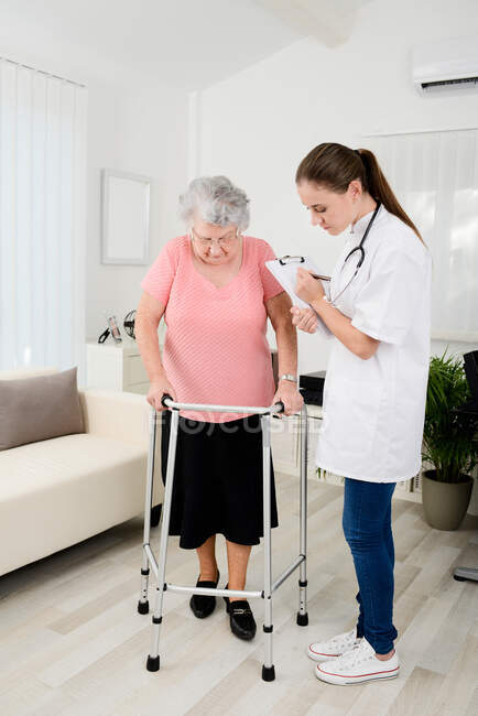 Jeune médecin vérifiant les progrès médicaux de réadaptation à la femme âgée à la maison. — Photo de stock