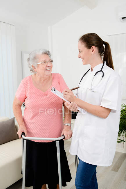 Jeune médecin vérifiant les progrès médicaux de réadaptation à la femme âgée à la maison. — Photo de stock