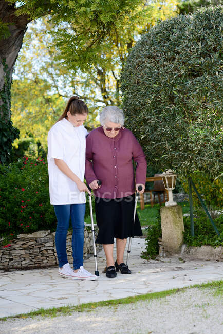 Elderly senior woman with a nurse walking outdoor in nursing home hospital garden — Stock Photo