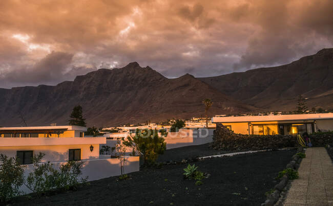 España, Islas Canarias, Isla Lanzarote, puesta de sol sobre las casas de Caleta de Famara - foto de stock