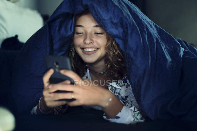 Дівчинка-підліток і повсякденне життя. У ліжку зі смартфоном — стокове фото