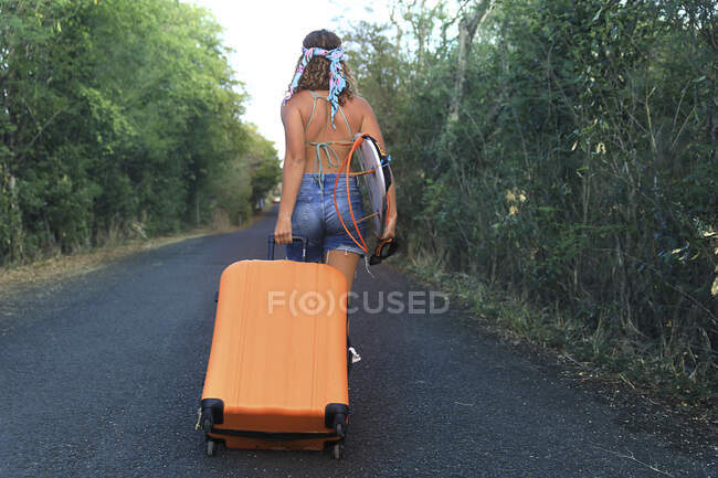 Uma rapariga com uma mala. Jovem e muito hippie em uma estrada deserta — Fotografia de Stock