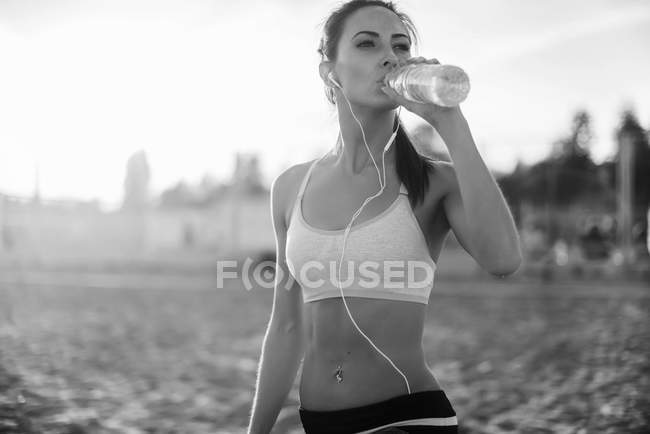 Belle athlète de fitness femme au repos l'eau potable après l'exercice sur la plage soirée d'été sous le soleil ensoleillé portrait en plein air — Photo de stock