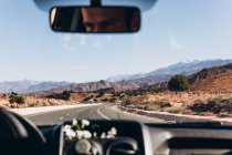 Reflexión en espejo de hombre conduciendo coche en carretera entre majestuosas montañas en Marruecos, África - foto de stock