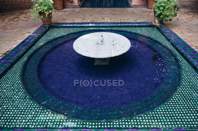 Vue grand angle de belle fontaine décorative avec des tuiles lumineuses et des plantes en pot dans la cour, Maroc, Afrique — Photo de stock