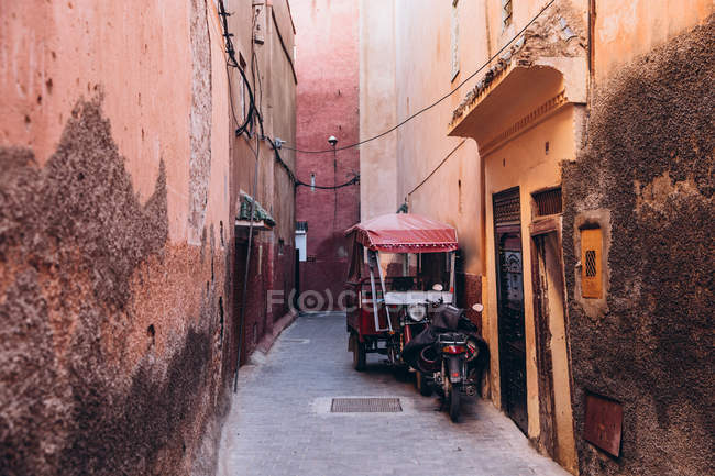 Estrecha calle entre casas antiguas y transporte local estacionado fuera en Marruecos, África - foto de stock