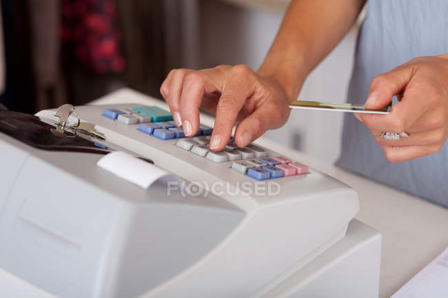 Saleswoman tenant la carte de crédit tout en utilisant la caisse — Photo de stock