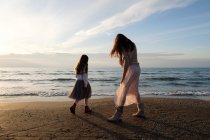 Visão traseira da mãe com a filha de pé na praia contra o céu com nuvens — Fotografia de Stock