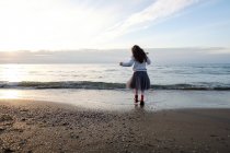 Rückansicht eines Mädchens, das am Strand steht und aufs Meer blickt — Stockfoto