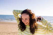 Смеющаяся молодая женщина с наушниками слушает музыку на пляже, избирательный фокус — стоковое фото