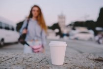 White plastic cup of coffee, woman in background — Stock Photo