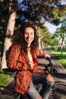 Молода жінка в помаранчевій куртці сидить на велосипеді, зосередитися на передньому плані — стокове фото