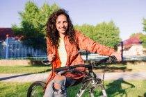 Молода жінка в помаранчевій куртці сидить на велосипеді, зосередитися на передньому плані — стокове фото