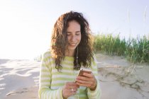 Молода жінка слухає музику зі смартфона на пляжі, фокус на передньому плані — стокове фото