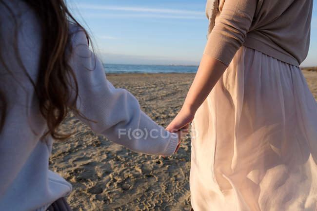 Vista recortada de la madre con la hija cogida de la mano mientras camina en la playa - foto de stock