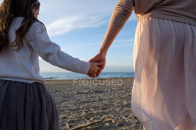 Обрізаний вид матері з дочкою тримає руки під час прогулянки на пляжі — стокове фото